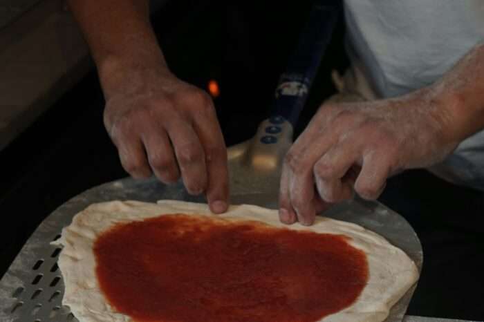 Person bereitet Pizzateig mit Tomatensauce zu.