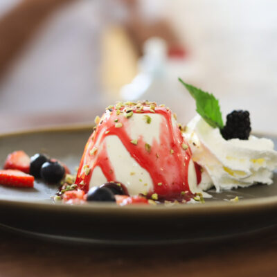 Panna cotta mit Früchten und Sahne auf Teller.