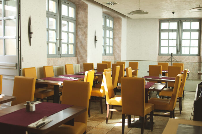 Leeres Restaurant mit gelben Stühlen und gedeckten Tischen.