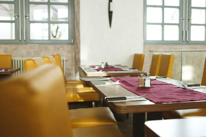 Leeres Restaurant mit gedeckten Tischen und gelben Stühlen.